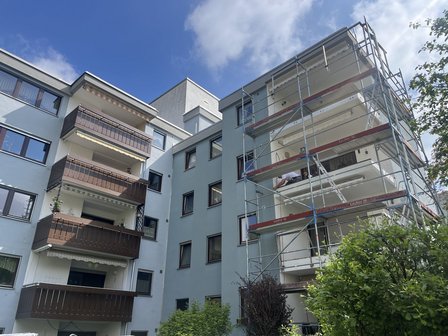 Mehrfamilienhaus mit Baugeruest an Balkonen, Arbeiter arbeitet am Balkonunterbau.