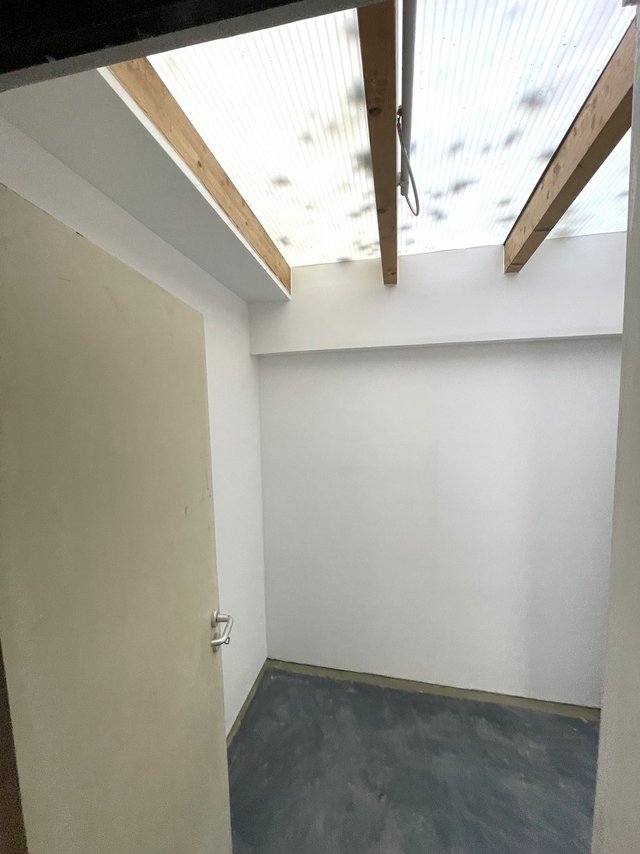 Kleiner leerer Raum mit weißen Wänden, Holzbalken und Dach aus lichtdurchlässigen Wellplatten