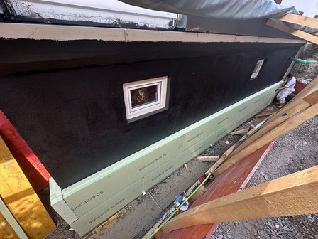 Arbeiter montiert helle Dämmplatten an schwarz beschichteter Kellerwand.