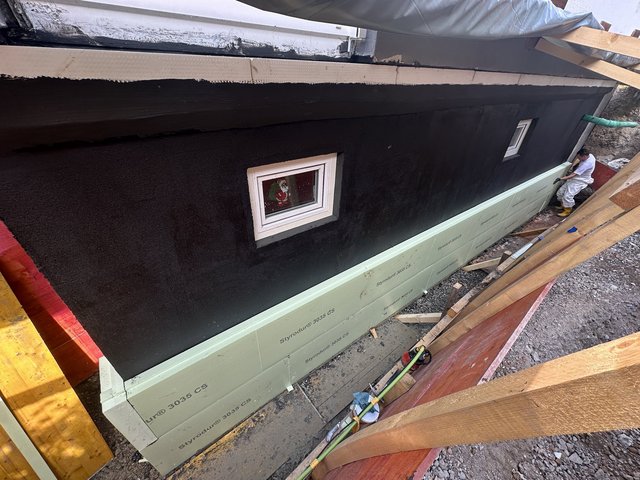 Arbeiter montiert helle Dämmplatten an schwarz beschichteter Kellerwand.