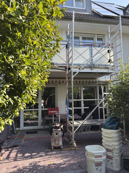 Geruest steht vor Balkonfassade eines Wohnhauses, Eimer und Bohrgeraet auf Terrasse