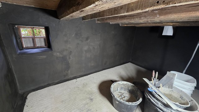 Dunkler Kellerraum mit verputzten Wänden, kleinem Fenster und Eimern mit Spachtelwerkzeugen auf Boden
