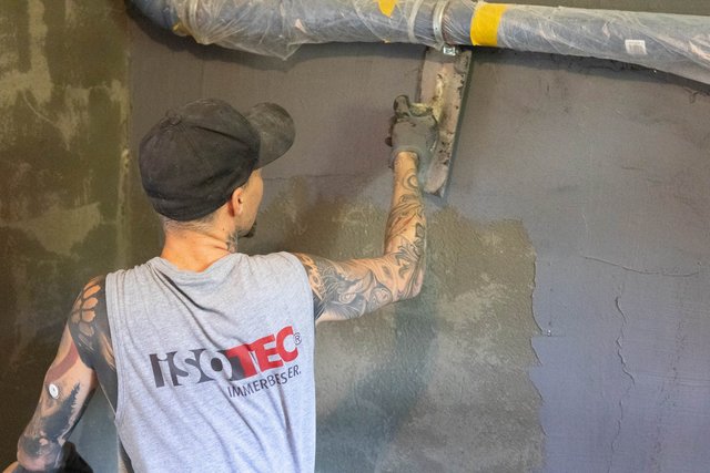 ISOTEC Mitarbeiter trägt graue Masse auf Kellerwand auf.