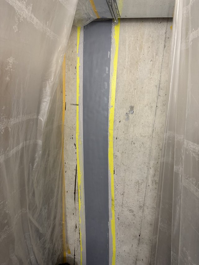 Graue Masse auf Betonwand, Bereich mit Folie und Klebeband abgeklebt