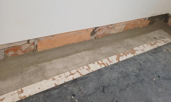 Freigelegter Mauerfuß mit rotem Ziegel, grauer Masse und Bodenfolie im Zimmer