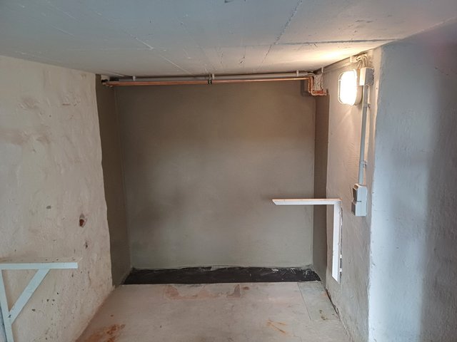 Glatte graue Wand in Kellerraum mit Leitungen