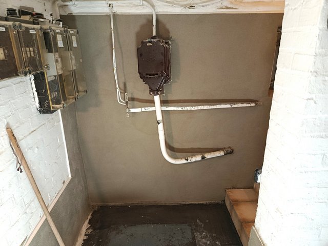 Kellerwand mit grauer Masse beschichtet, Leitungen und Sicherungskästen sichtbar
