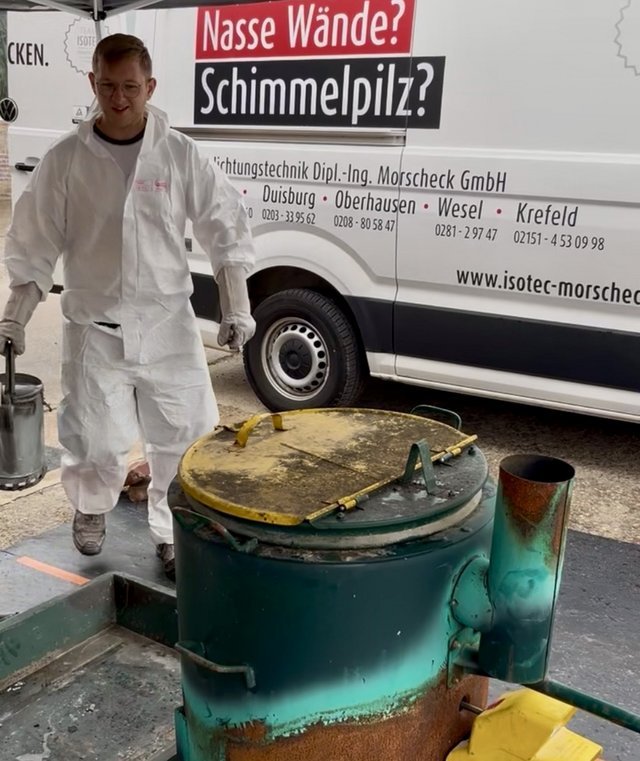 ISOTEC Mitarbeiter in Schutzanzug steht neben Brennofen vor Firmenfahrzeug.
