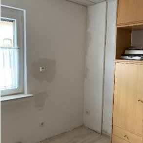 Helles Zimmer mit verfärbter Wand neben Fenster und Holzschrank
