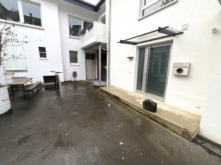 Nasser Innenhof mit weißer Hausfassade, Eingangstür und Betonstufe