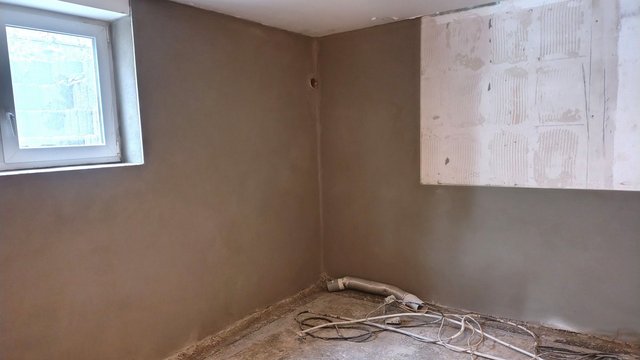 Graue Masse auf Kellerwand, Fenster links, Kabel und Rohr am Boden