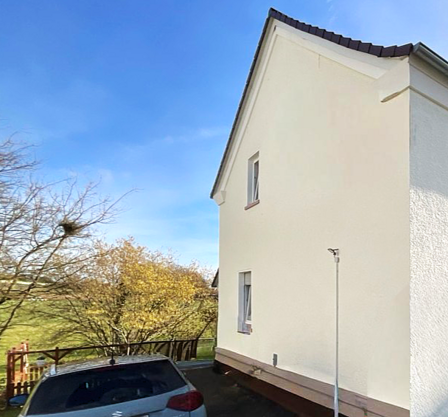 Helle Hausfassade mit zwei Fenstern und geparktem Auto im Außenbereich