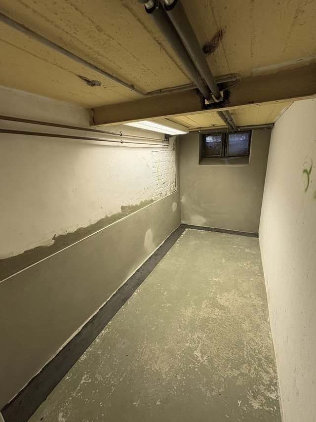 Kellerraum mit Rohrleitungen an der Decke und grauer Masse am unteren Wandbereich.