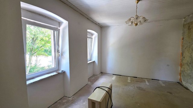 Leerer Raum mit zwei Fenstern, weißer Decke, Rohboden und freigelegter grauer Wandkante