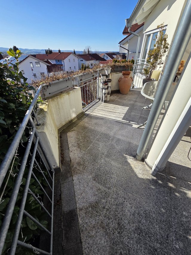 Balkon mit grauen Fliesen, Geländer und Blick auf Häuser unter blauem Himmel
