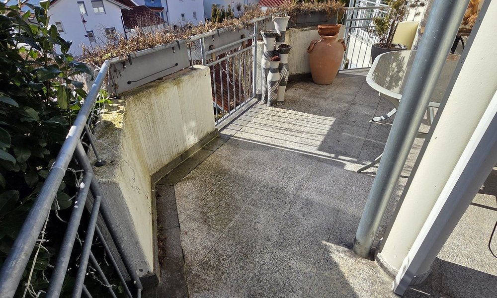 Balkon mit grauen Fliesen, Geländer und Blick auf Häuser unter blauem Himmel