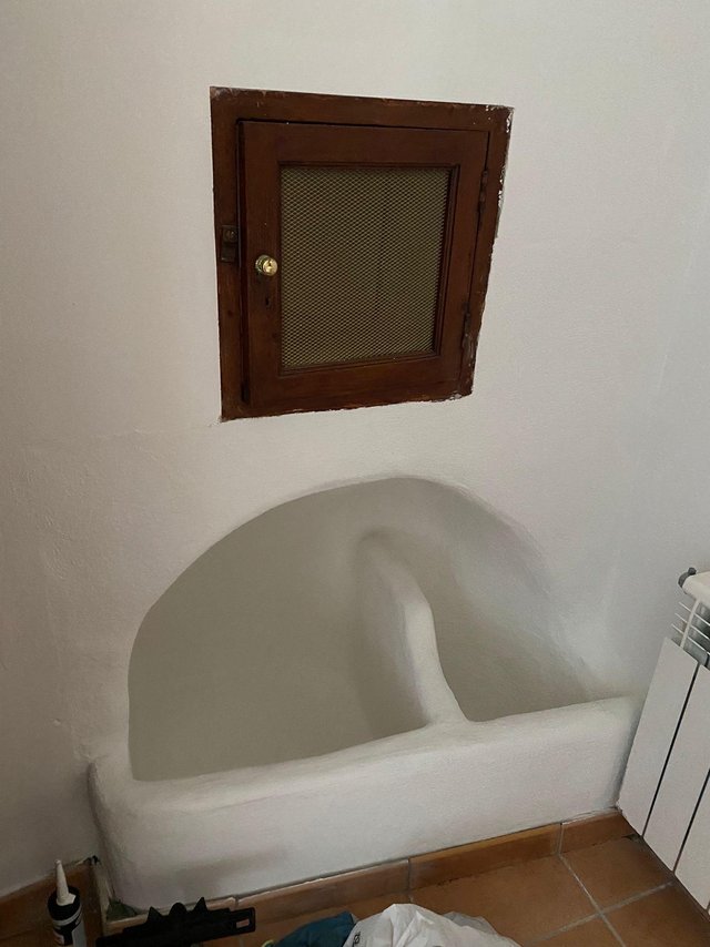 Kleine Holzklappe mit Metallgitter an weißer Wand über Badewanne