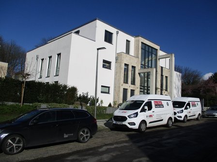 ISOTEC Transporter stehen vor modernem Wohngebäude mit großer Glasfront.
