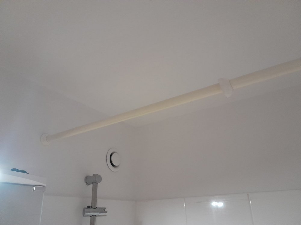 Weiße Decke mit Rohrleitung, Lüftungsöffnung und Duschstange im Badezimmer