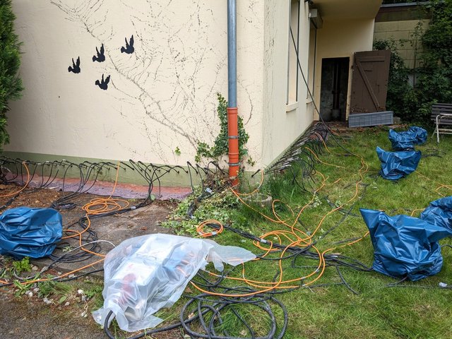 Kabel und Schläuche liegen am Hausfundament entlang, teils mit Folie abgedeckt.