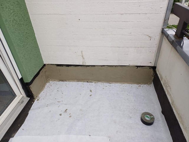 Graue Masse an Wandanschluss auf Balkon, Bodenfläche mit weißem Vlies abgedeckt
