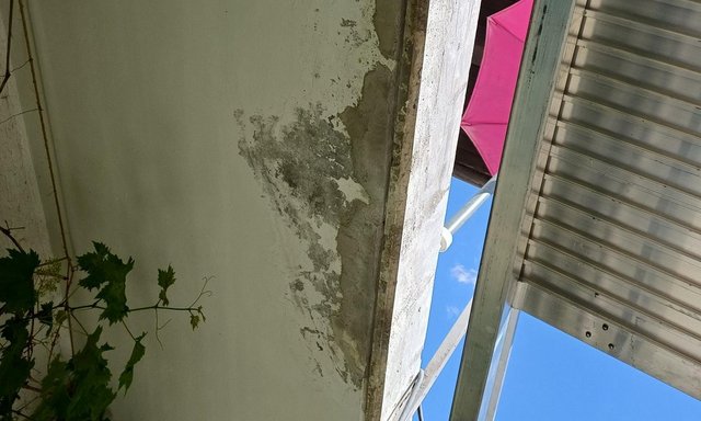 Graue Schadstelle an Deckenrand neben Metallgeruest, Blick nach oben.