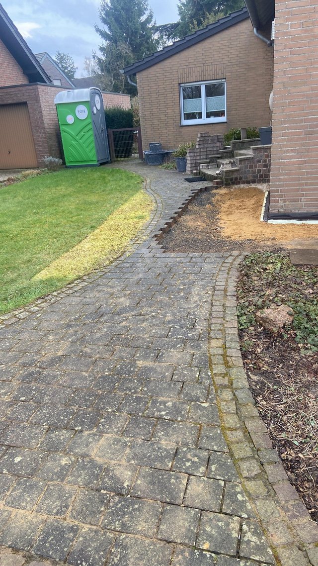 Freigelegter Erdstreifen entlang Hauswand neben gepflastertem Weg