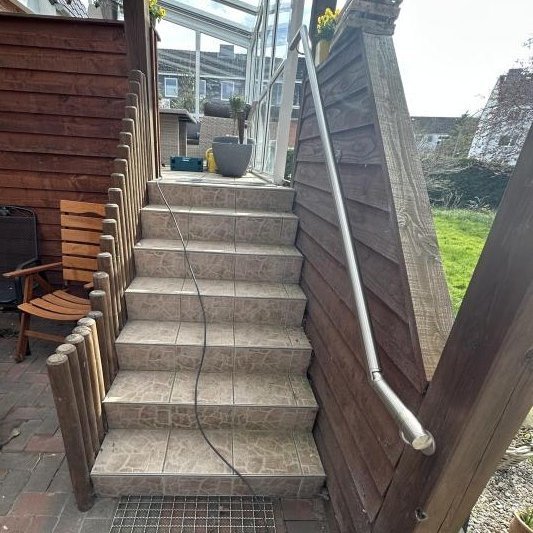 Geflieste Treppe mit Metallhandlauf, Kabel liegt über den Stufen, Glasüberdachung darüber.