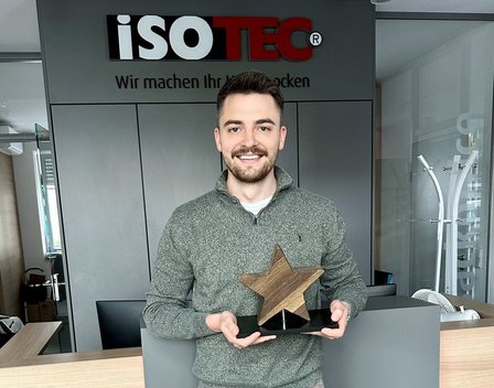 ISOTEC Mitarbeiter hält Sternpokal aus Holz an Empfangstresen im Büro.