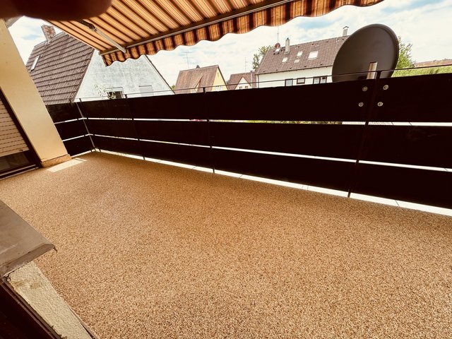 Balkon mit Markise, schwarzer Brüstung und Blick auf Hausdächer und Satellitenschüssel