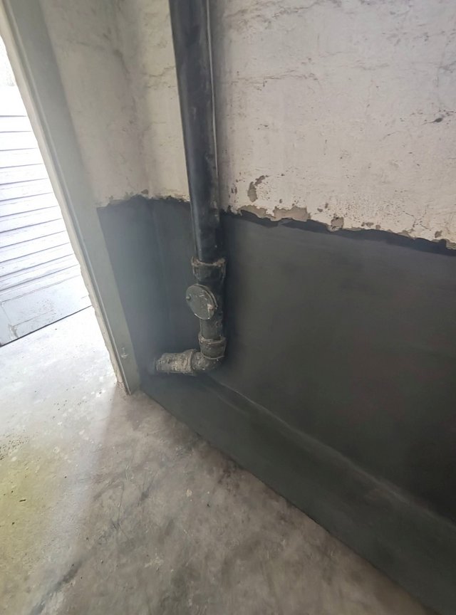 Schwarze Masse an Wand mit Abflussrohr im Sockelbereich