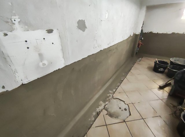 Graue Masse auf Kellerwand aufgetragen, gefliester Raum mit Eimern und Besen