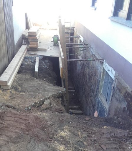 Aushubgraben entlang Gebäudewand mit freigelegter Kellerwand und Abstützungen