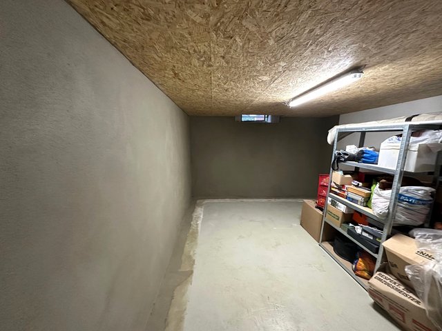 Kellerraum mit Betonboden, OSB-Decke, Regal mit Kartons und kleinem Fenster.