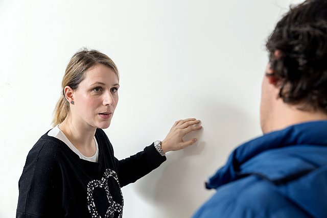Person zeigt auf glatte weiße Wand und spricht mit Gegenüber