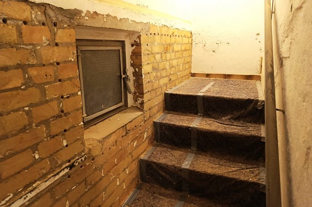 Freigelegte Ziegelwand mit Bohrlöchern an Treppenaufgang neben kleinem Fenster