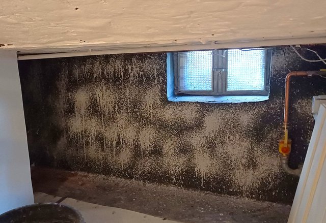 Dunkle Kellerwand mit großflächigen hellen Flecken unter kleinem Fenster