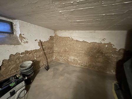 Abgeplatzte Wandbeschichtung im Kellerraum mit freigelegter brauner Fläche