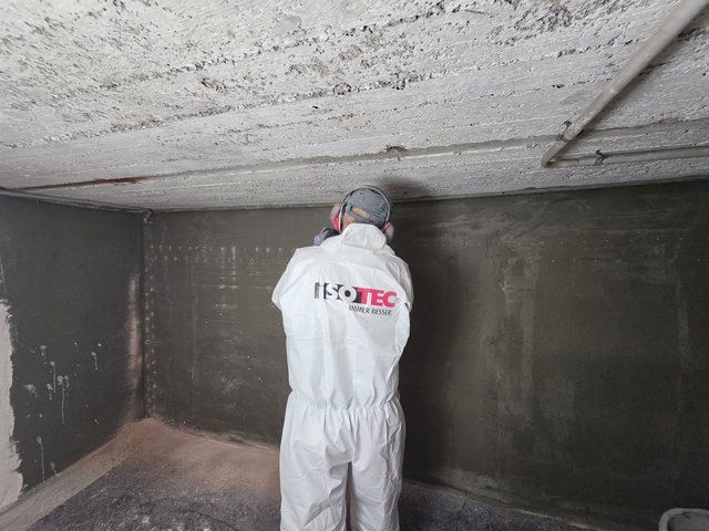 ISOTEC Mitarbeiter prüft schwarze Masse an Kellerwand.