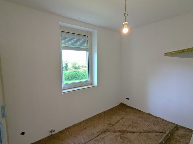 Leerer Raum mit Fenster, Glühbirne an Kabel und rauem Bodenaufbau