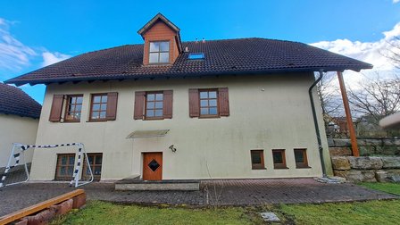 Zweigeschossiges Haus mit braunem Ziegeldach, Holzfenstern und gepflasterter Terrasse