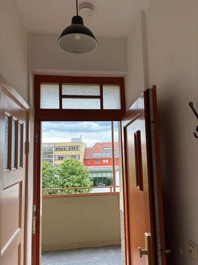 Offene Wohnungstuer im Flur, Blick auf Balkon und Gebaeude bei Tageslicht
