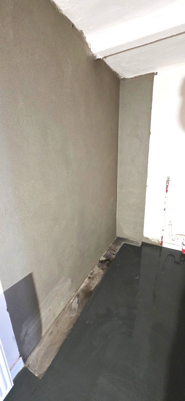 Schwarze Bodenbeschichtung in schmalem Raum neben grauer Wand