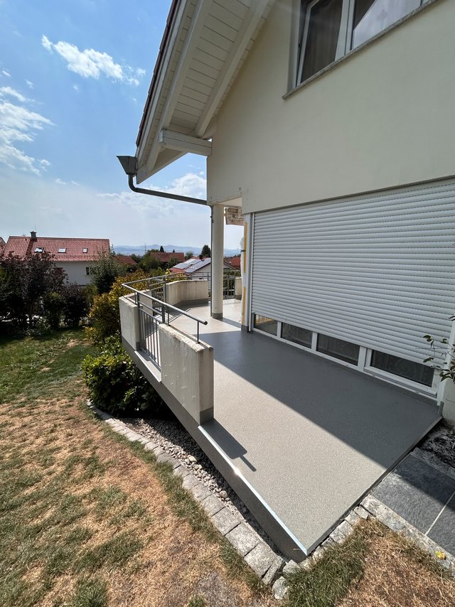 Beton-Balkon mit Metallgeländer an Hausfassade, Blick auf Garten und Dächer