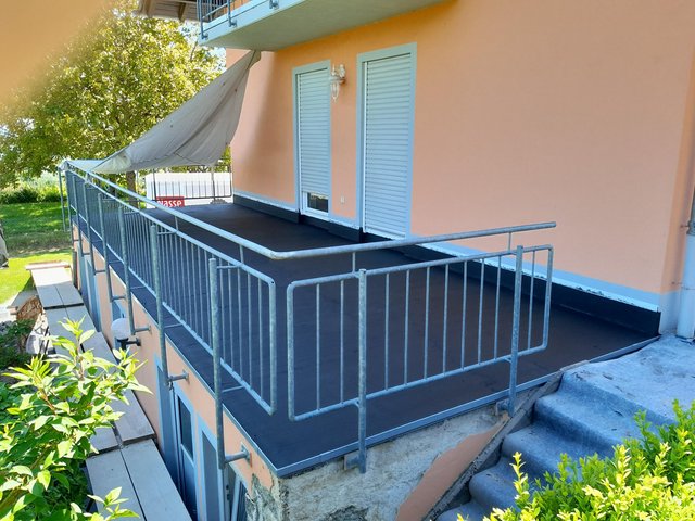 Balkon mit dunkler Beschichtung, Metallgeländer und Markise vor Fensterläden
