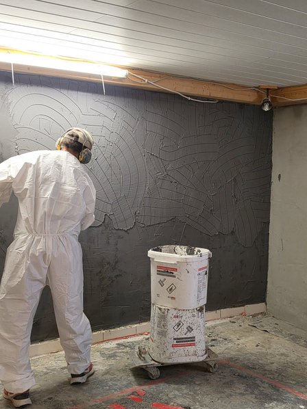 ISOTEC Mitarbeiter trägt graue Masse auf Kellerwand auf.