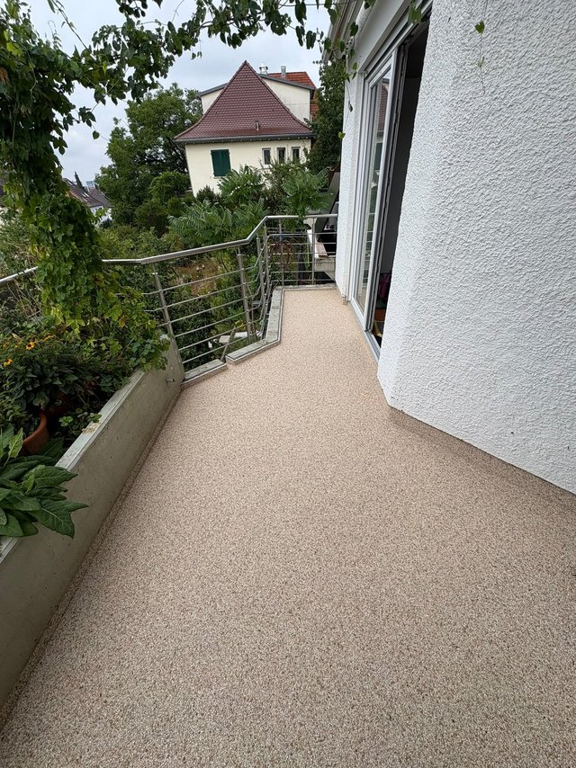Balkon mit hellem Bodenbelag, Metallgeländer und Pflanzen, Blick auf Nachbarhaus.