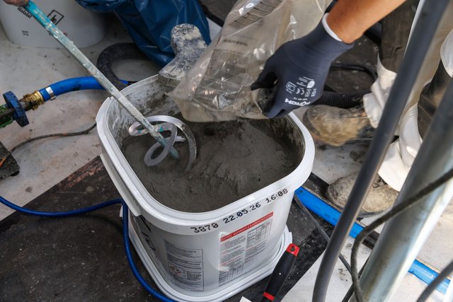 ISOTEC Mitarbeiter schüttet graues Pulver in Eimer mit Rührquirl.