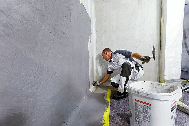 ISOTEC Mitarbeiter trägt graue Masse auf Wand im Raum auf.