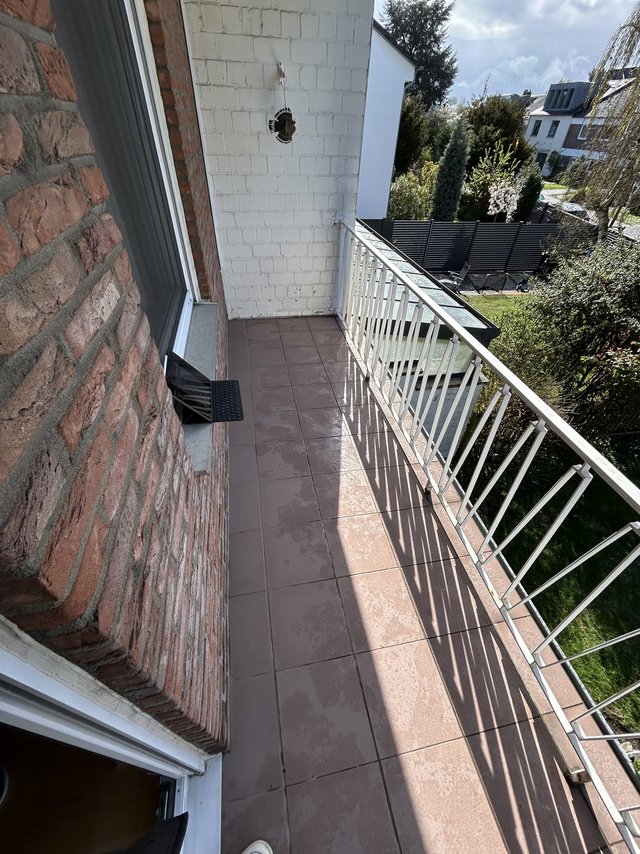 Schmaler Balkon mit Fliesenboden, Metallgeländer und Bohrloch in weißer Wand